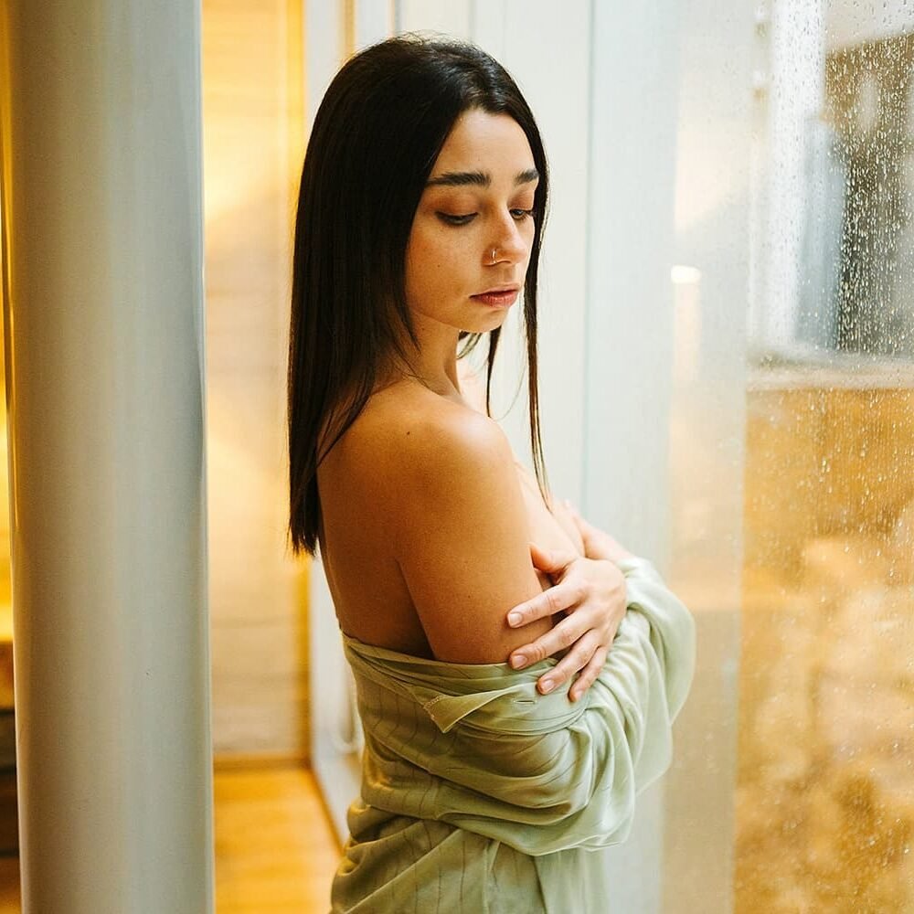 Ericka Benítez junto a una ventana con lluvia, con una camisa abierta sobre los hombros.