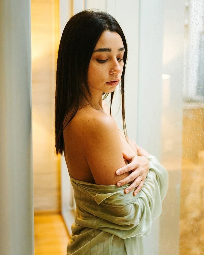 Ericka Benítez junto a una ventana con lluvia, con una camisa abierta sobre los hombros.